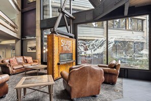 A spacious lounge area with leather sofas, a coffee table, and a fireplace labeled 'SILVER KING.' Large windows provide a view of a snowy landscape. - Beautiful 3BR Park City Mountain Basecamp | Walk to Lifts, Pool, Hot Tub & Sauna (Park City)