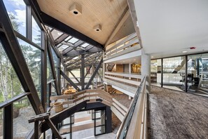 Een meerlaags interieur met een houten trap, glazen balustrades en uitzicht op het buitengebied.
