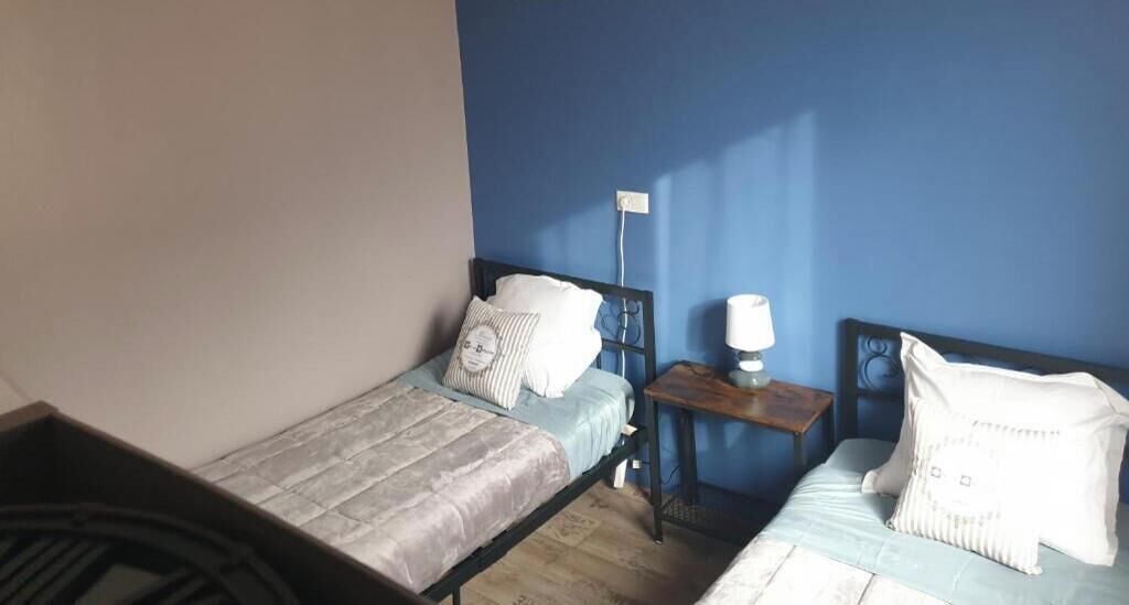 Une petite pièce avec deux lits, une table de chevet et une prise électrique au mur.