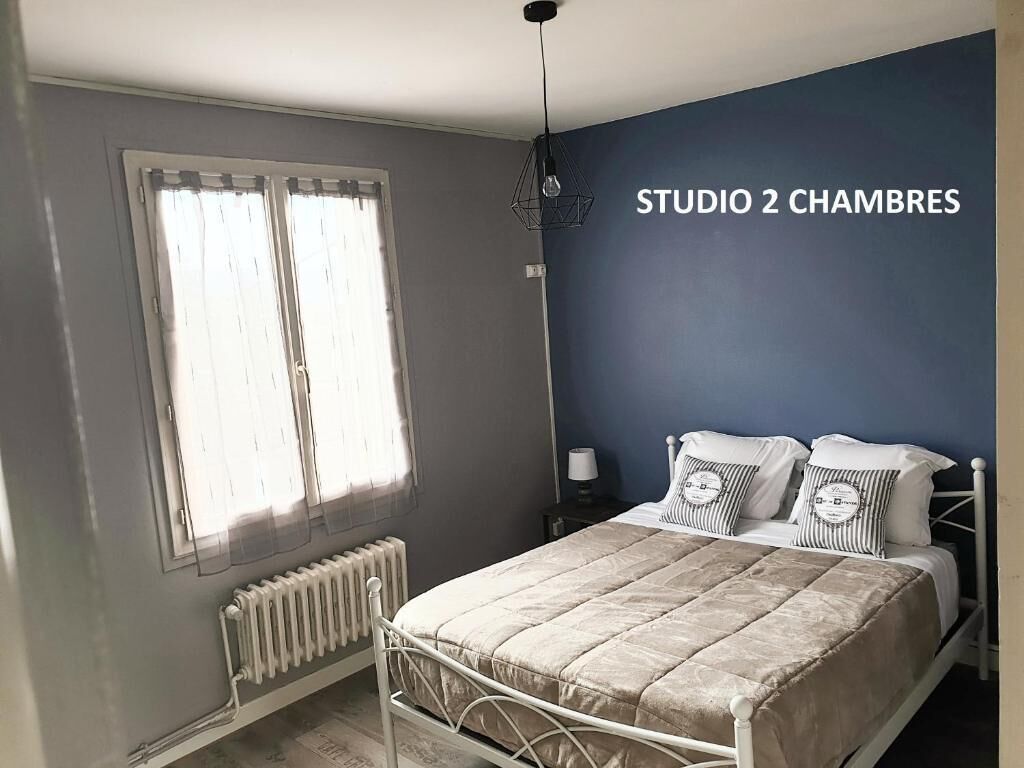 Ett sovrum med en säng, ett element, ett fönster med gardiner och en vägg med texten ”STUDIO 2 CHAMBRES”.