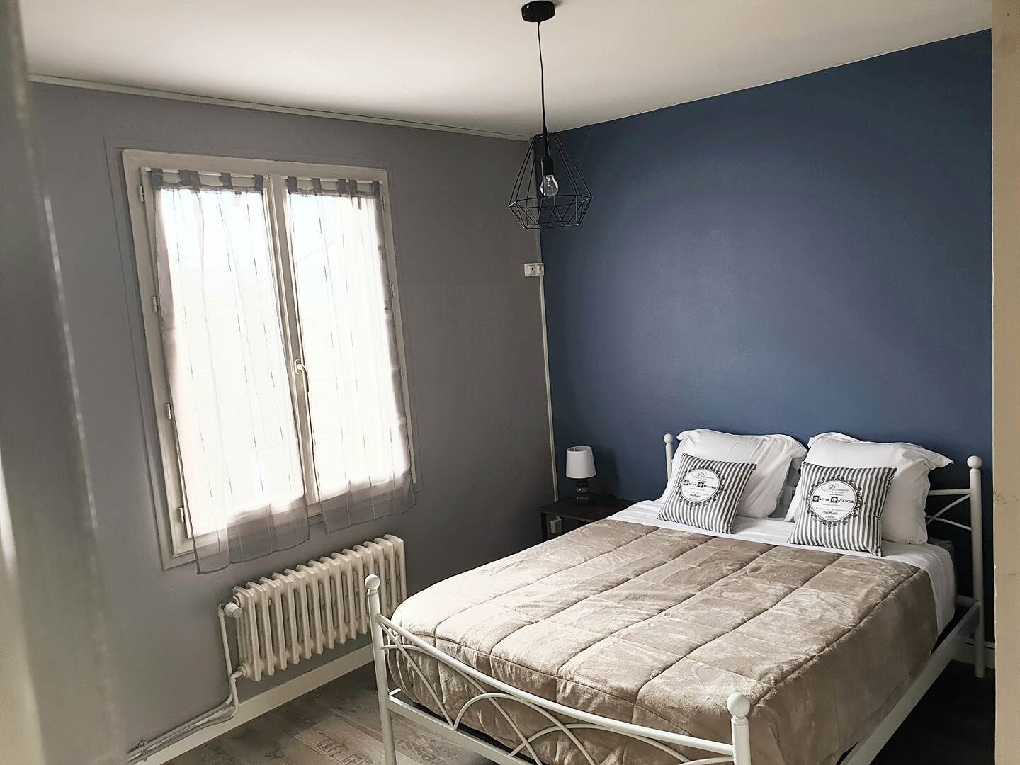 Un dormitorio con cama, radiador, ventana con cortinas y una lámpara de pared.