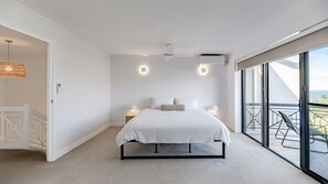 Un dormitorio moderno con una cama grande, lámparas de noche, un ventilador de techo y un balcón con vistas.