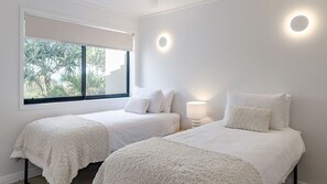 Ein Schlafzimmer mit zwei Betten, einem Fenster mit Blick auf Palmen und einer Wandleuchte.