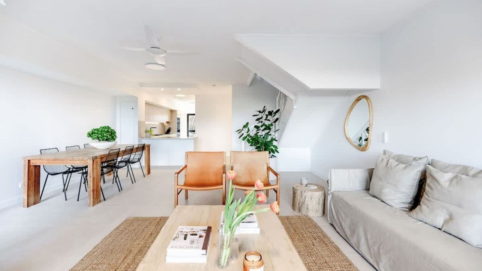 A modern living room with a sofa, coffee table, and chairs, a dining area with a table and chairs, and a kitchen in the background.