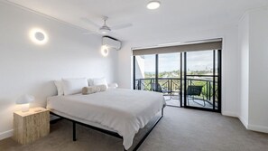 Ein Schlafzimmer mit Bett, Nachttisch, Lampe, Deckenventilator, Klimaanlage und einem Balkon mit Blick.