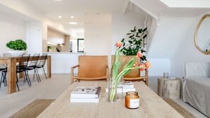 Ein modernes Wohnzimmer mit Couchtisch aus Holz, Büchern, einer Kerze und einer Vase mit Blumen.