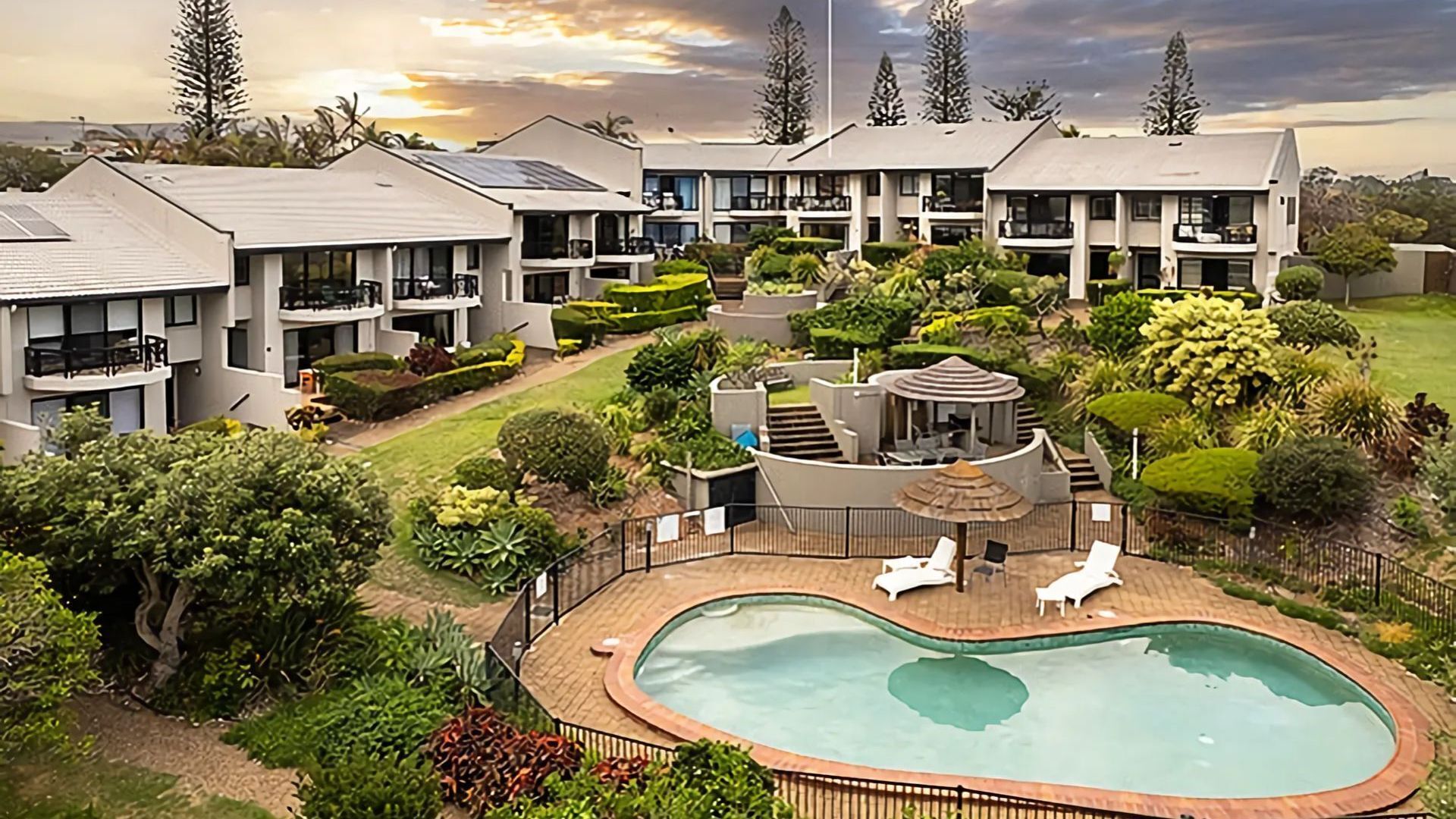 A residential complex with multiple apartment buildings, a swimming pool, and landscaped gardens.