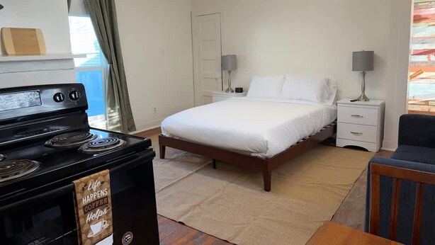 Une chambre à coucher avec un lit, des tables de chevet, une lampe, un poêle et une vue sur l’extérieur.