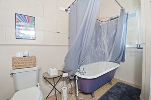 Ein Badezimmer mit Badewanne, Toilette und einem kleinen Tisch mit Korb und Toilettenpapier.