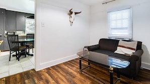 A living room with a glass coffee table, a black sofa, and a mounted animal skull on the wall. - Comfortable 3BR Home Near Downtown (Lafayette)