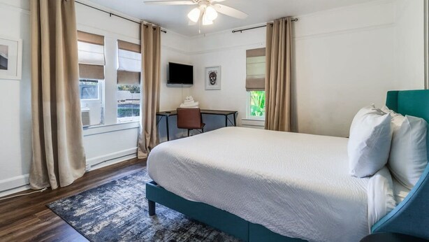 A bedroom with a bed, a desk, a chair, a ceiling fan, and a window with curtains. - Comfortable 3BR Home Near Downtown (Lafayette)