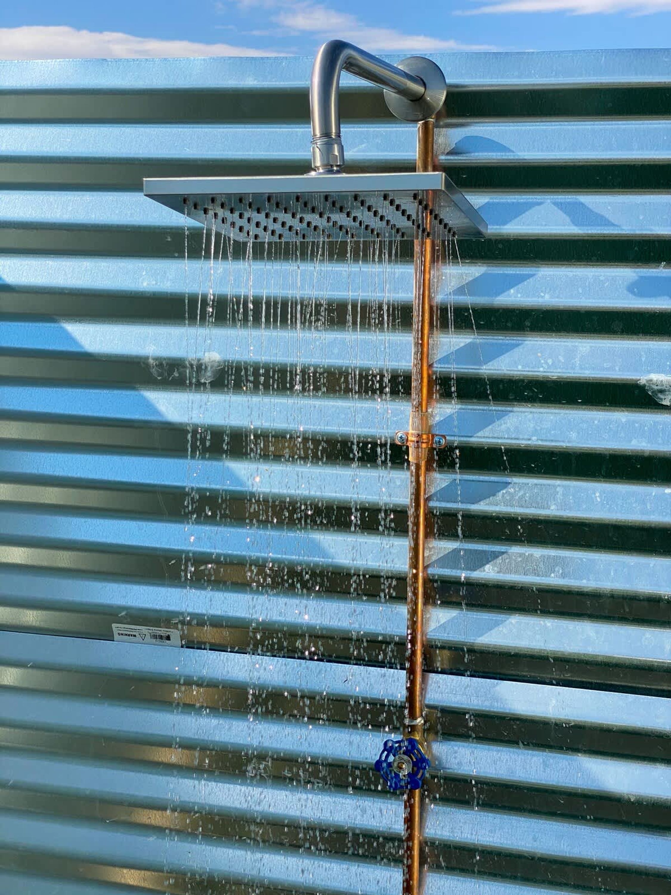 Een douchekop met stromend water tegen een golfplaten muur.