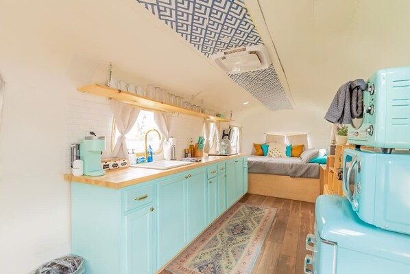 A compact kitchen with a central island, a bed with a patterned rug, and a vintage refrigerator.