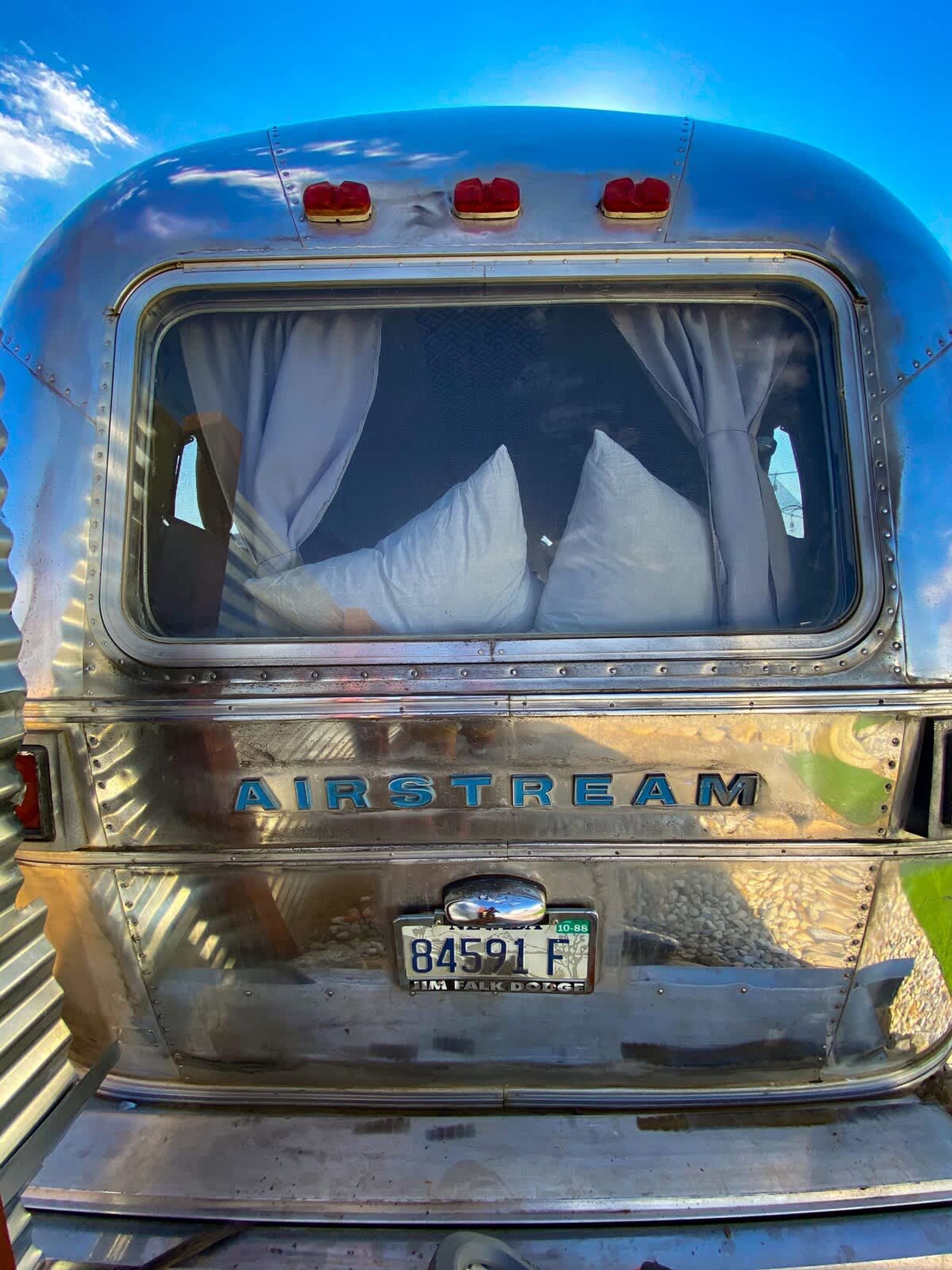 À l’arrière d’un autobus d’époque, on peut voir le mot « AIRSTREAM » peint à l’arrière, une plaque d’immatriculation et des rideaux visibles à travers la fenêtre.