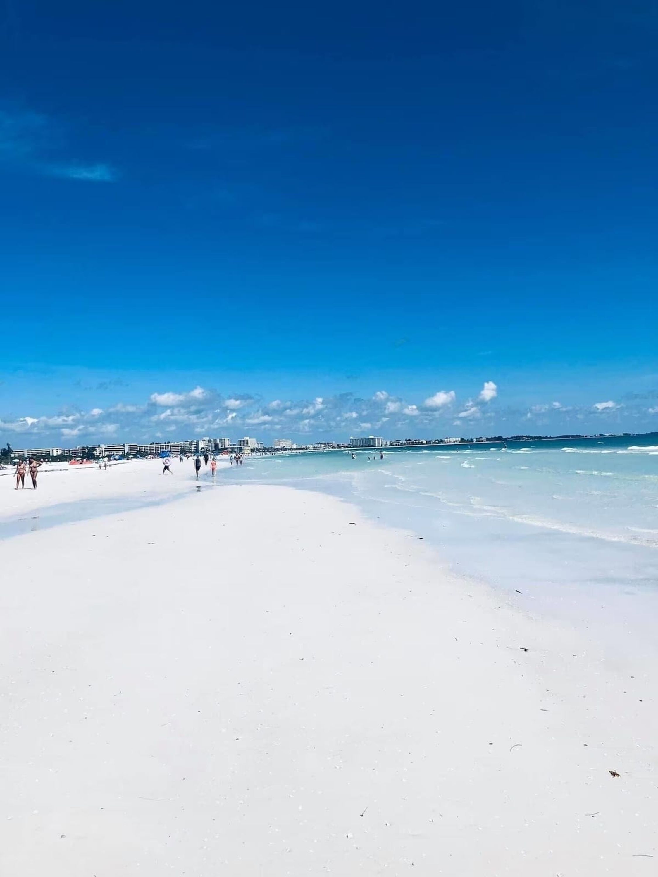 Une plage avec un ciel dégagé et quelques personnes qui se promènent sur le sable.