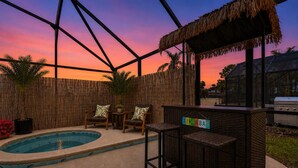 A pool area with a bar, chairs, and a thatched roof structure. - Your Private Resort Tiki Bar Near Disney (Kissimmee)
