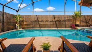 A swimming pool with a thatched roof structure overhead, surrounded by bamboo fencing and potted plants. - Your Private Resort Tiki Bar Near Disney (Kissimmee)