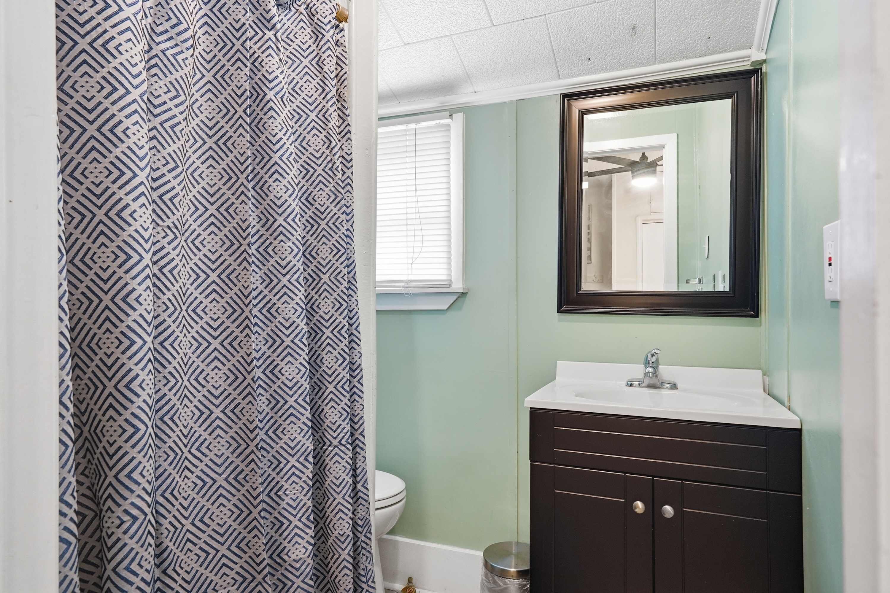 Une salle de bain avec un rideau de douche à motifs, un lavabo avec un miroir et des toilettes.