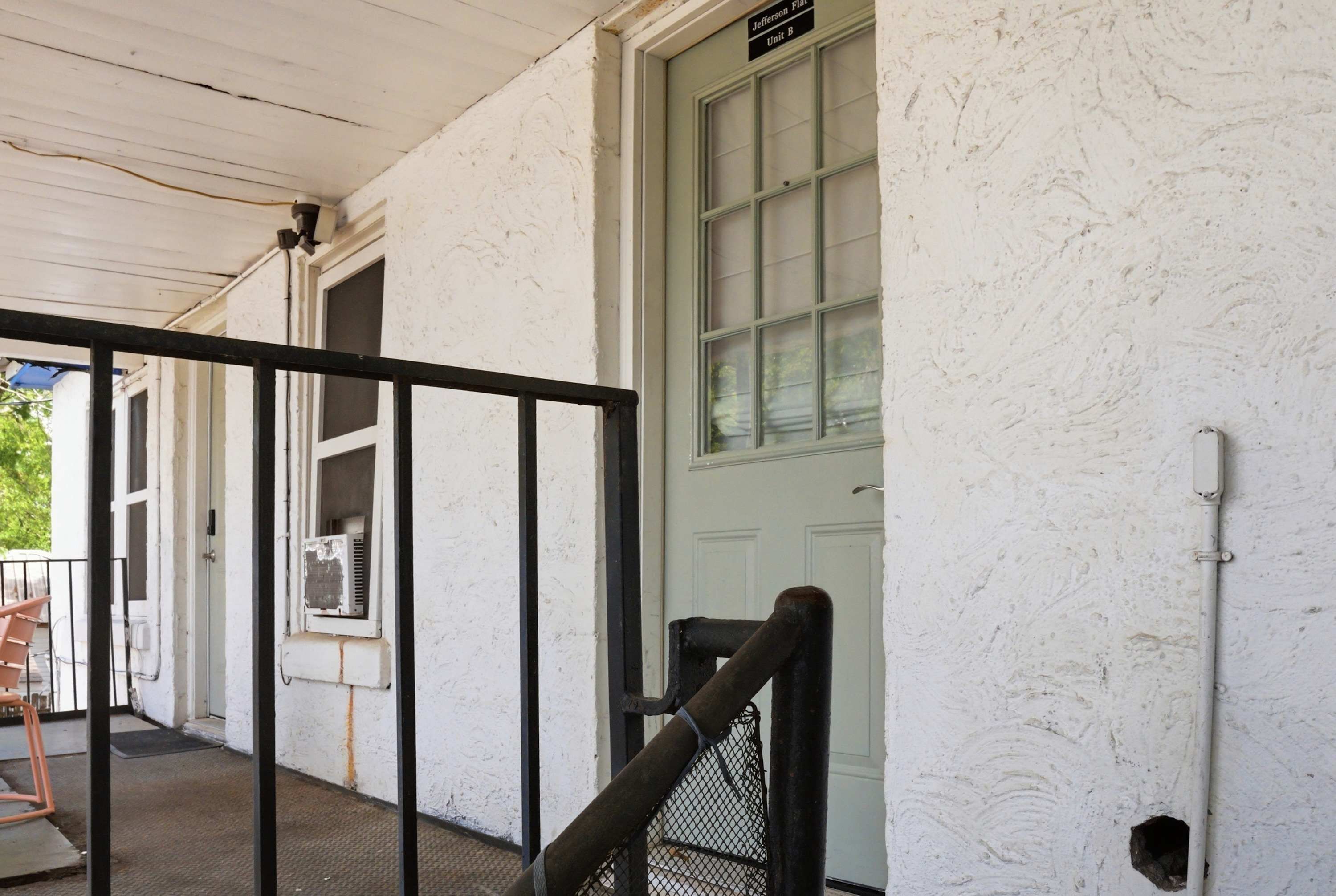 A white building with a green door, a black metal gate, and a small window with an air conditioning unit.