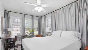 A bedroom with a bed, desk, chair, ceiling fan, and windows with curtains.