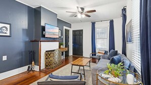 A living room with a sofa, a coffee table, a fireplace, a television, and a ceiling fan. - Affordable Private Room Near Downtown (Lafayette)