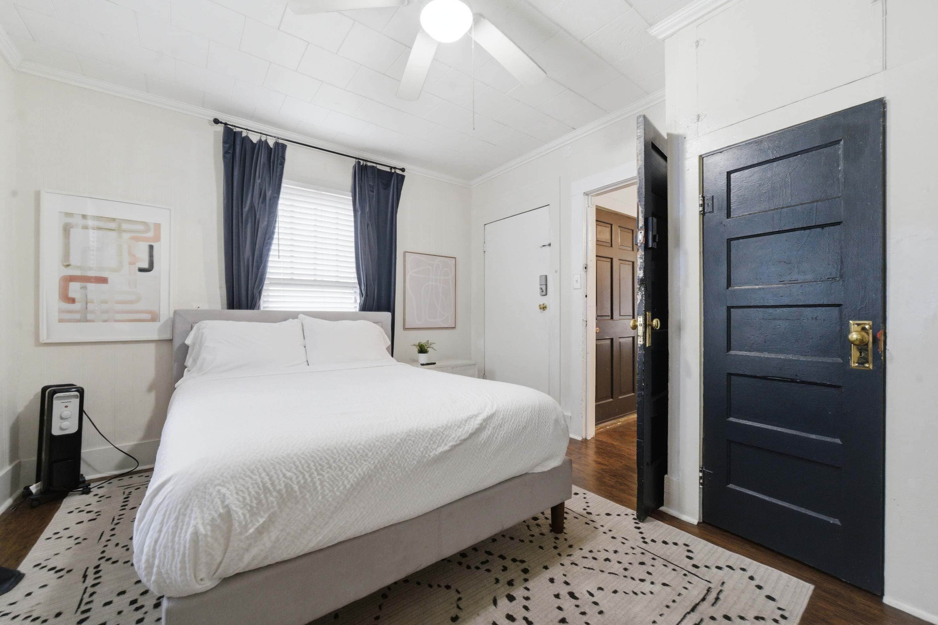A bedroom with a bed, a bedside table, a lamp, a door, and a window with curtains.