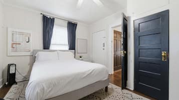 A bedroom with a bed, a bedside table, a lamp, a door, and a window with curtains.