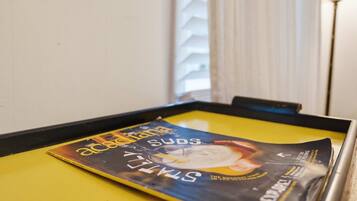 A table with a magazine on it, a window with blinds, and a lamp in the background.
