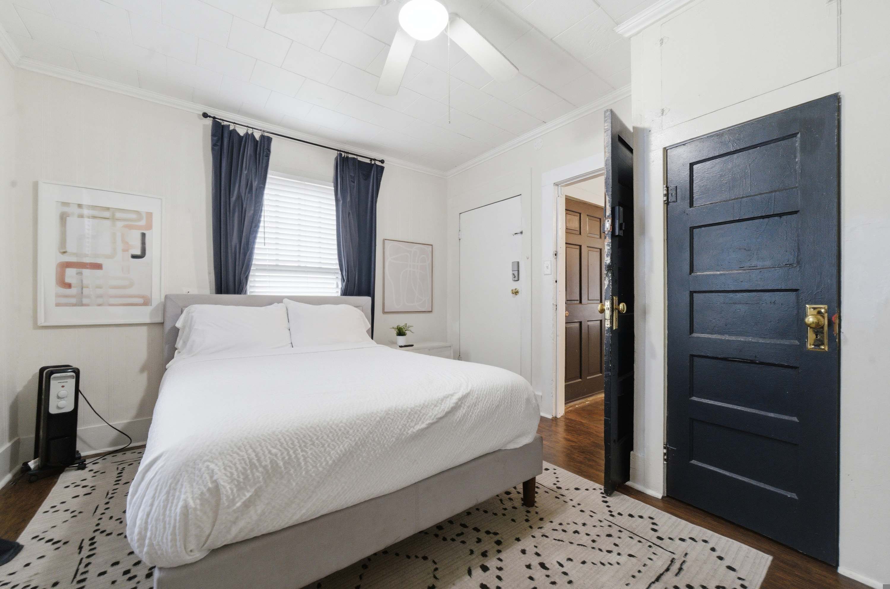 A bedroom with a bed, a bedside table, a lamp, a door, and a window with curtains.