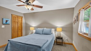 Ein Schlafzimmer mit einem Bett, einem Deckenventilator, zwei Nachttischlampen, einem Fenster mit Vorhängen und einem Holzschrank.