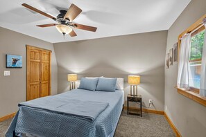 Ein Schlafzimmer mit einem Bett, einem Deckenventilator, zwei Nachttischlampen, einem Fenster mit Vorhängen und einem Holzschrank.