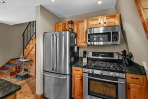 Una cocina con electrodomésticos de acero inoxidable, armarios de madera, microondas, estufa y refrigerador.