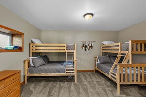 A room with two bunk beds, a wooden dresser, a wall-mounted shelf with books, and a ceiling light fixture. - Sunrise at Sugar - Fenced yard, hot tub, views, pet friendly (Sugar Mountain)