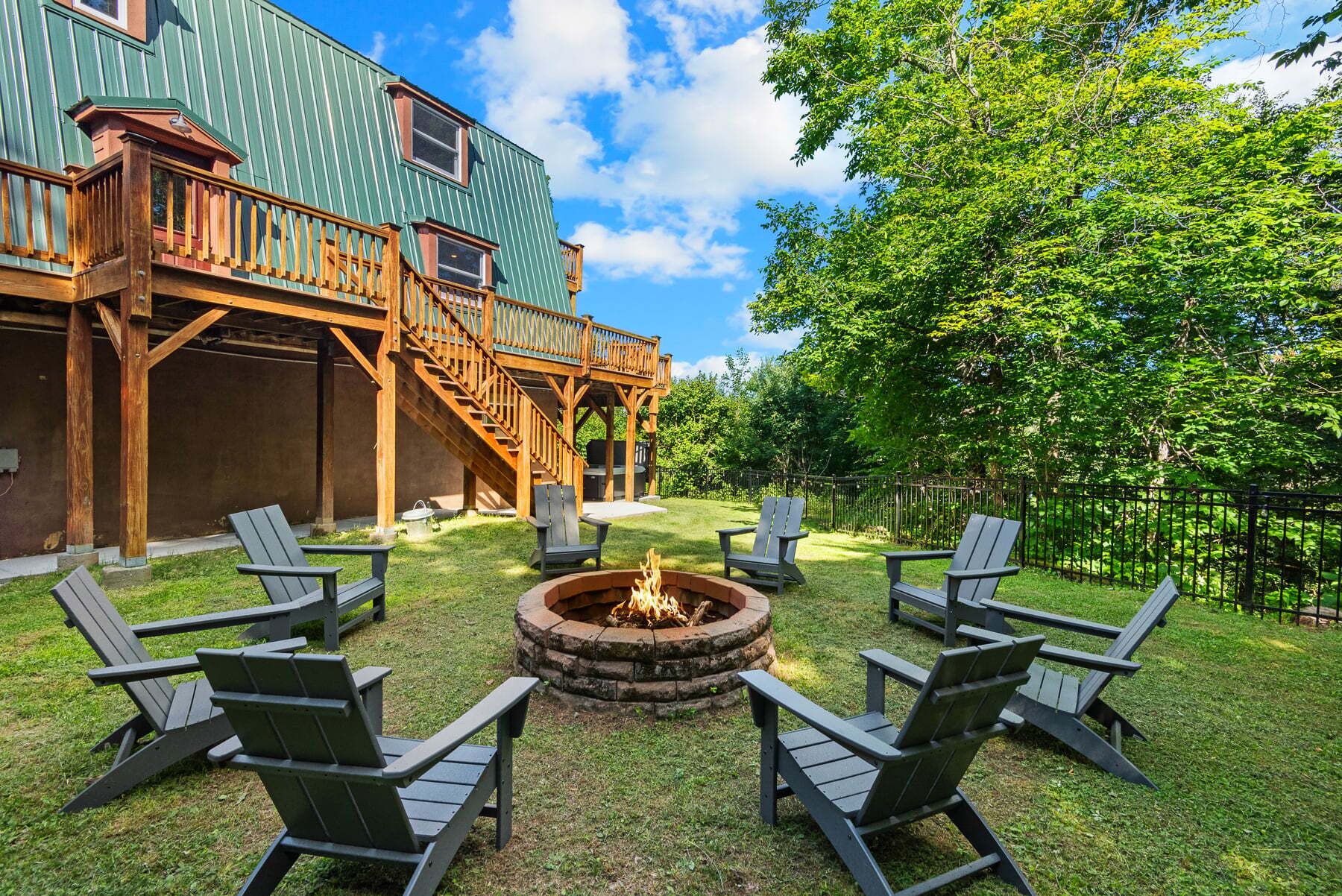 A backyard with a fire pit, outdoor seating, and a wooden deck.