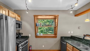 Eine kompakte Küche mit Einbauofen, Mikrowelle, Spüle und einem Fenster mit Blick auf Grünflächen.
