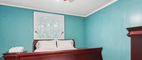 A bedroom with a bed, a nightstand, a dresser, a ceiling fan, and a window with blinds.
