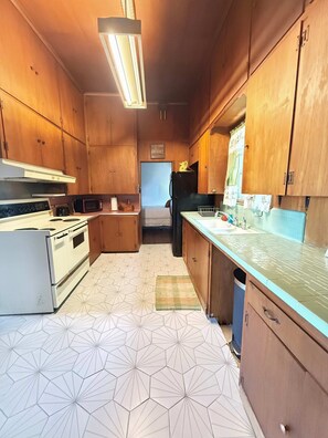 Eine kompakte Küche mit Holzausstattung, einer Mikrowelle, einem Kühlschrank und einem fußbodenbelag mit Muster.