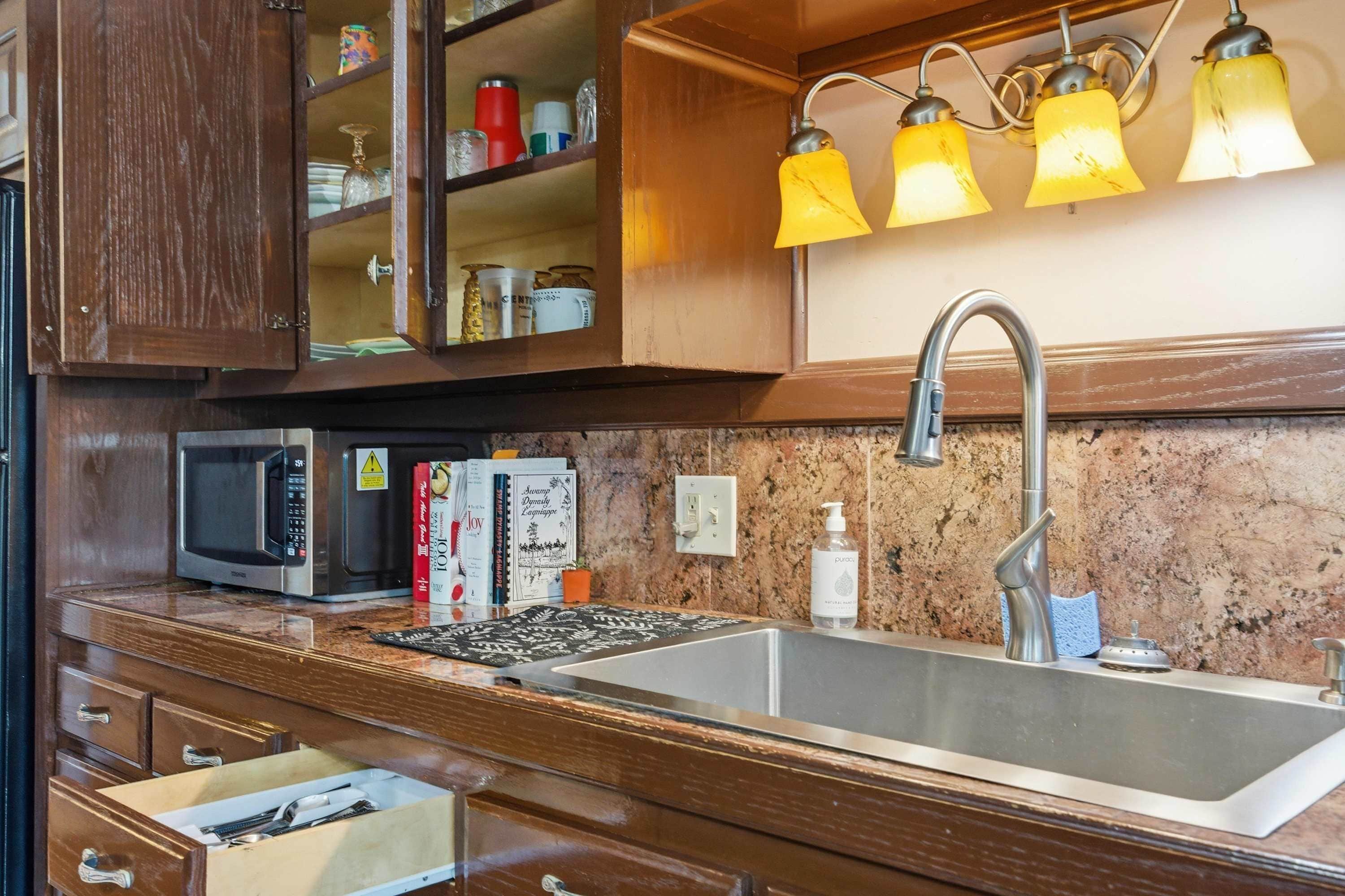 Una cocina con armarios de madera, un lavamanos de acero inoxidable, un microondas y un conjunto de lámparas colgantes amarillas.