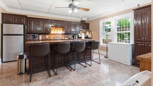 A kitchen with a central island, bar stools, a refrigerator, microwave, and a window with a view.