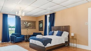 Ett hotellrum med en stor säng, ett skrivbord, en stol, en kristallkrona och konstverk på väggarna.