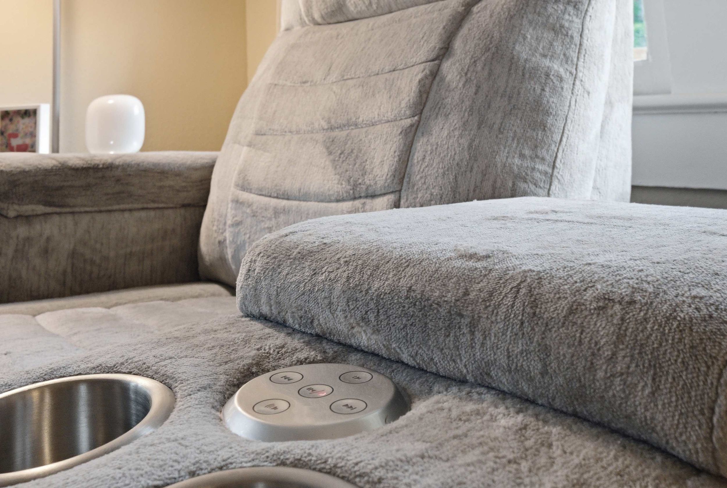A section of a grey upholstered sofa with a metallic tray and control panel.