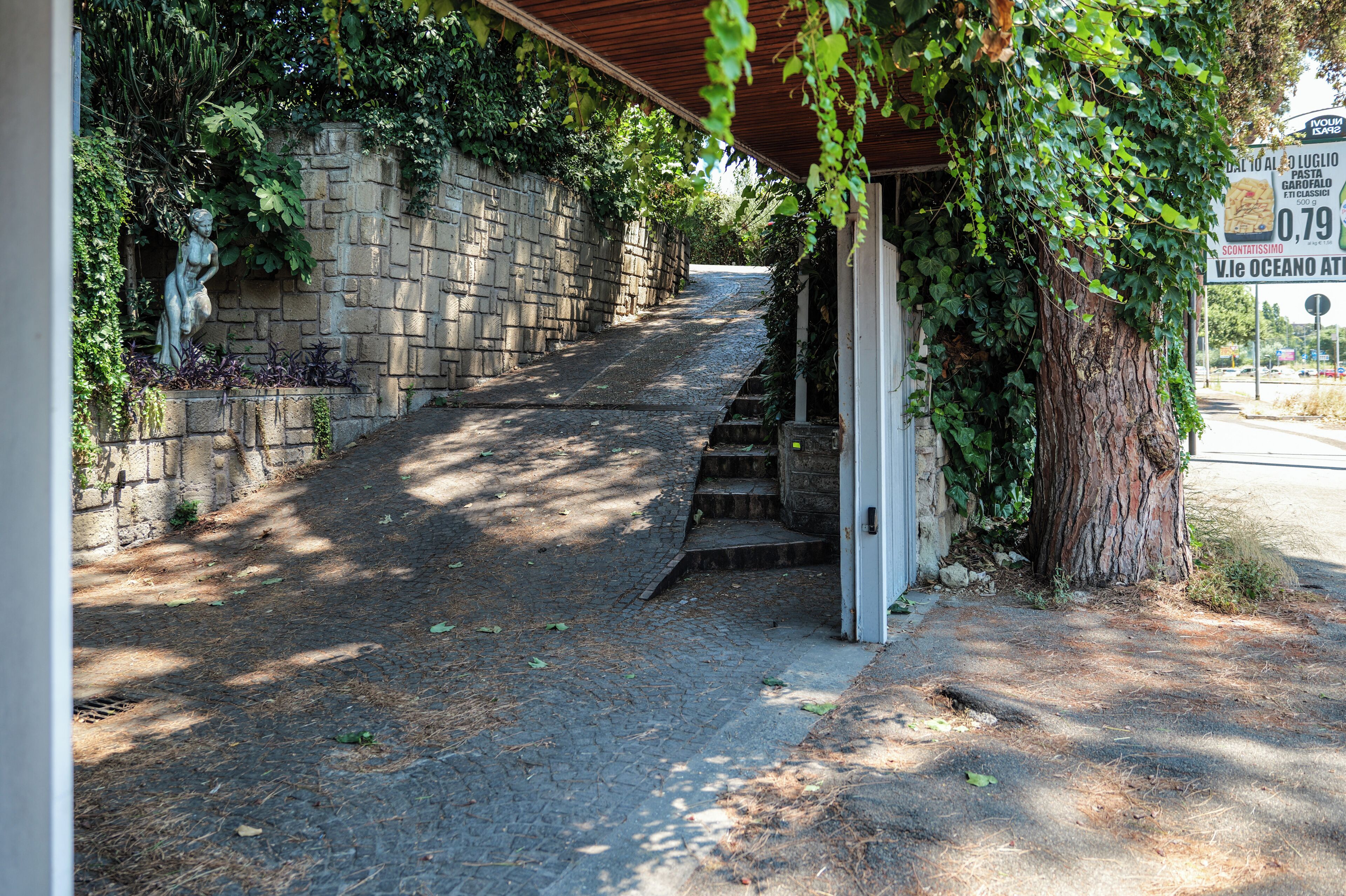 Un escalier en pierre menant à l’entrée d’un bâtiment, entouré de verdure et d’un mur de pierre.
