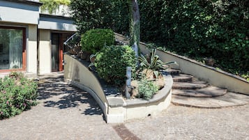 Ein gepflasterter Weg führt zu einem Gebäude mit geschwungenem Eingang, umgeben von Grünflächen und einem kleinen Garten.