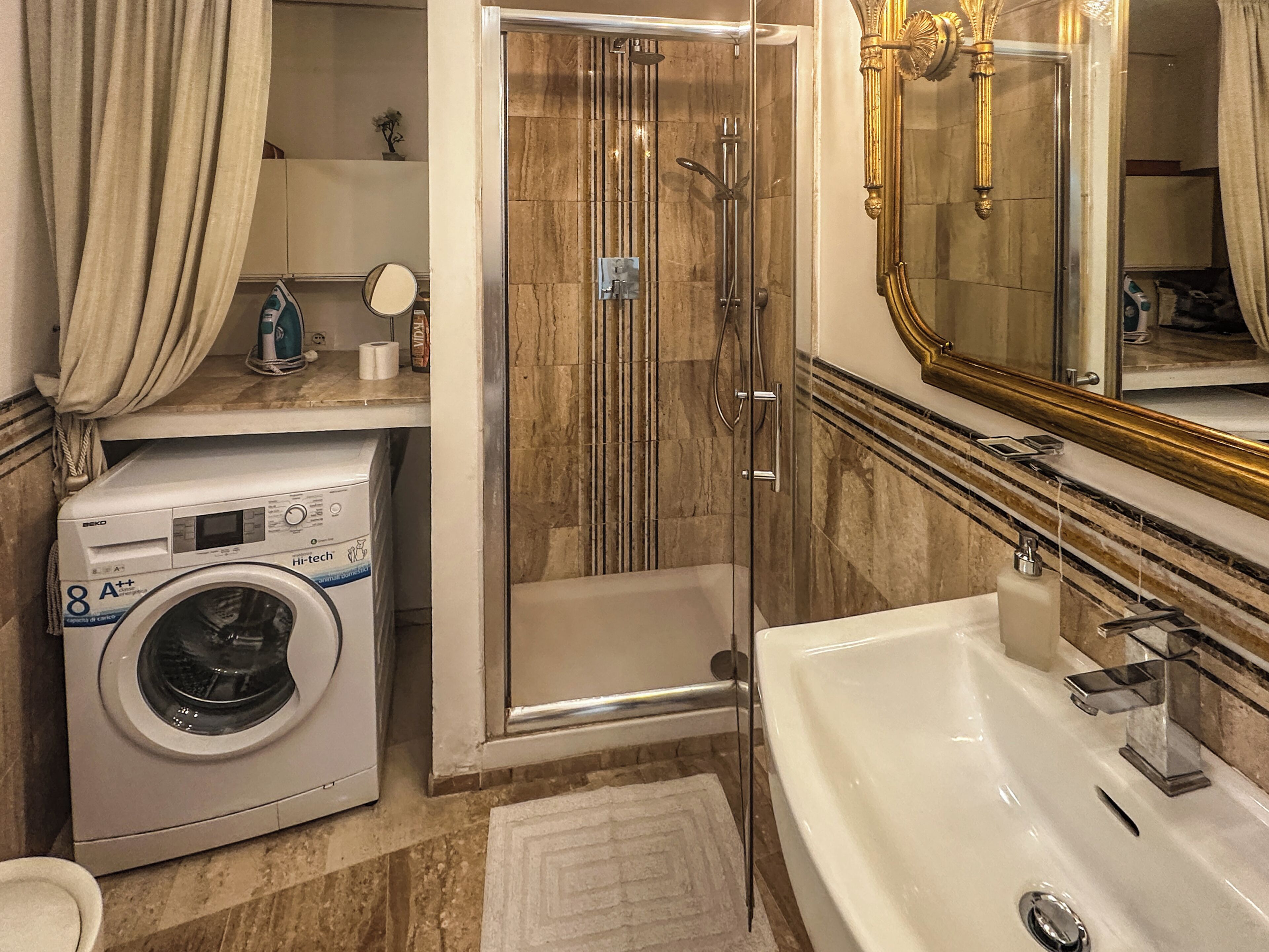 A bathroom with a washing machine, a glass-enclosed shower, a bathtub, and a large mirror.