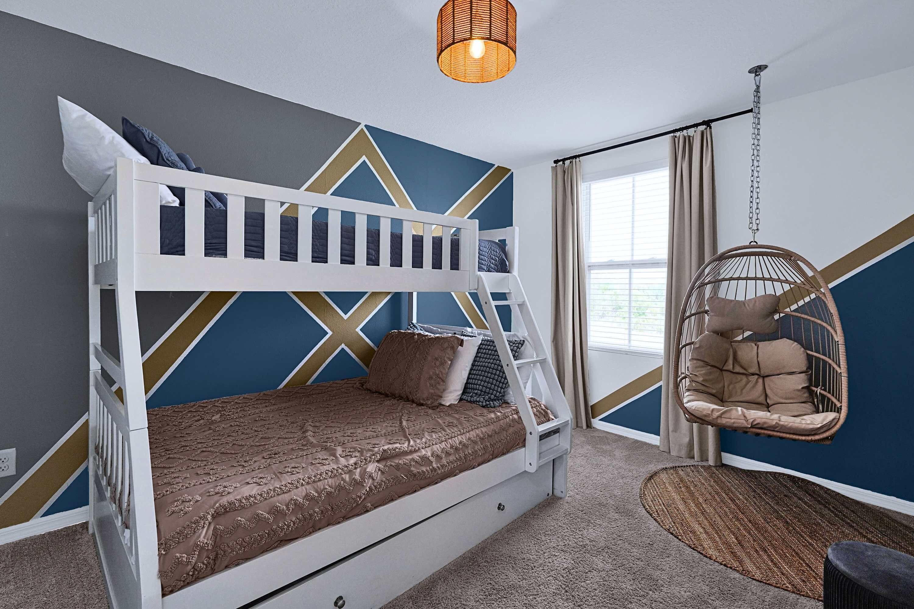 A bunk bed with a patterned bedspread, a hanging chair, and a geometric wall design.