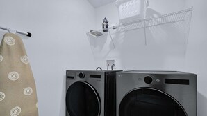 A laundry area with two stacked washers and dryers, a drying rack, and a towel hanging on a rack.
