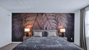A bedroom with a large bed, two bedside lamps, a dark patterned wall, and a window with curtains.