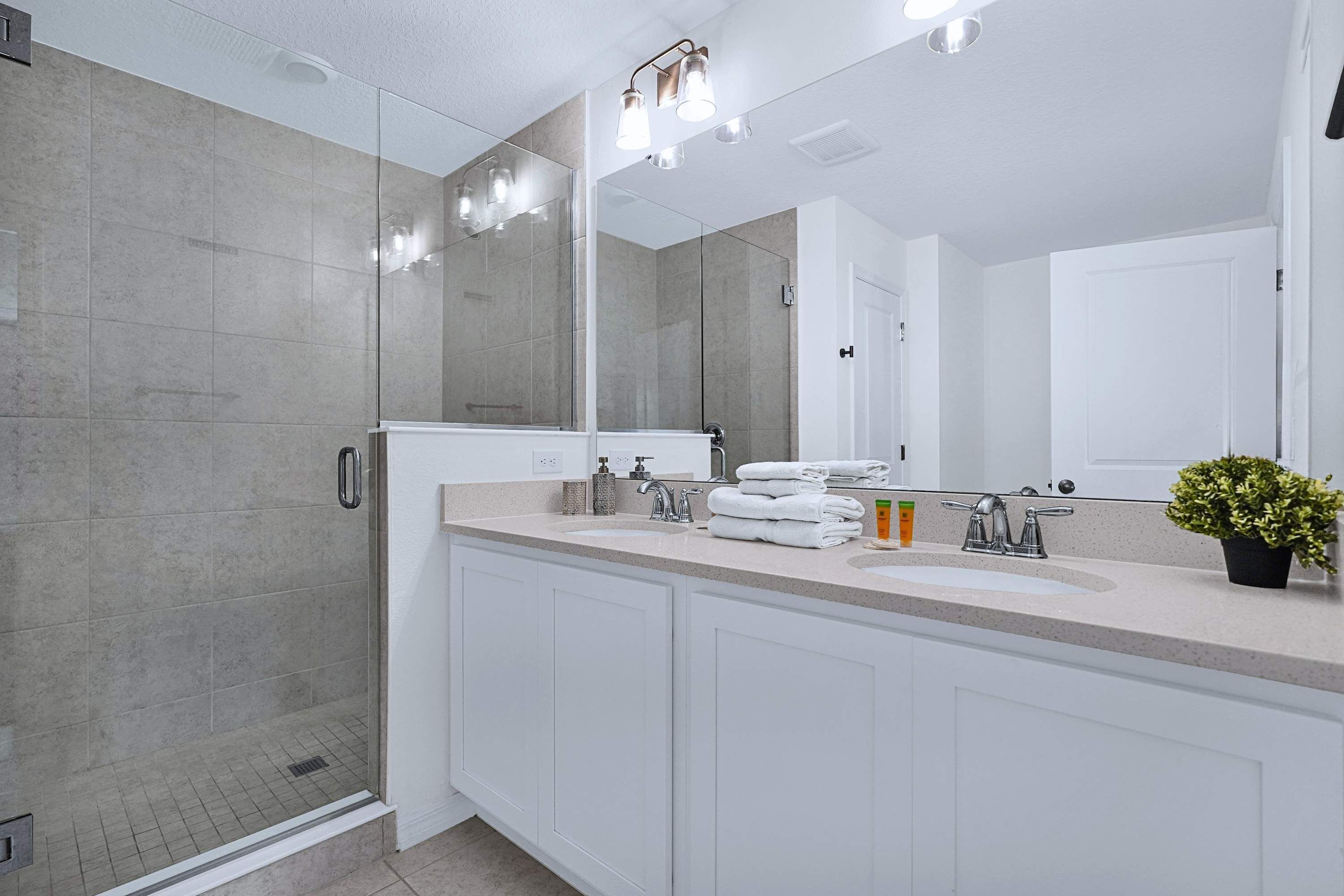 A modern bathroom with a glass shower enclosure, a large mirror, and a countertop with a sink and towel stack.