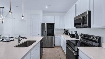 A modern kitchen with white cabinets, stainless steel appliances, and pendant lighting.
