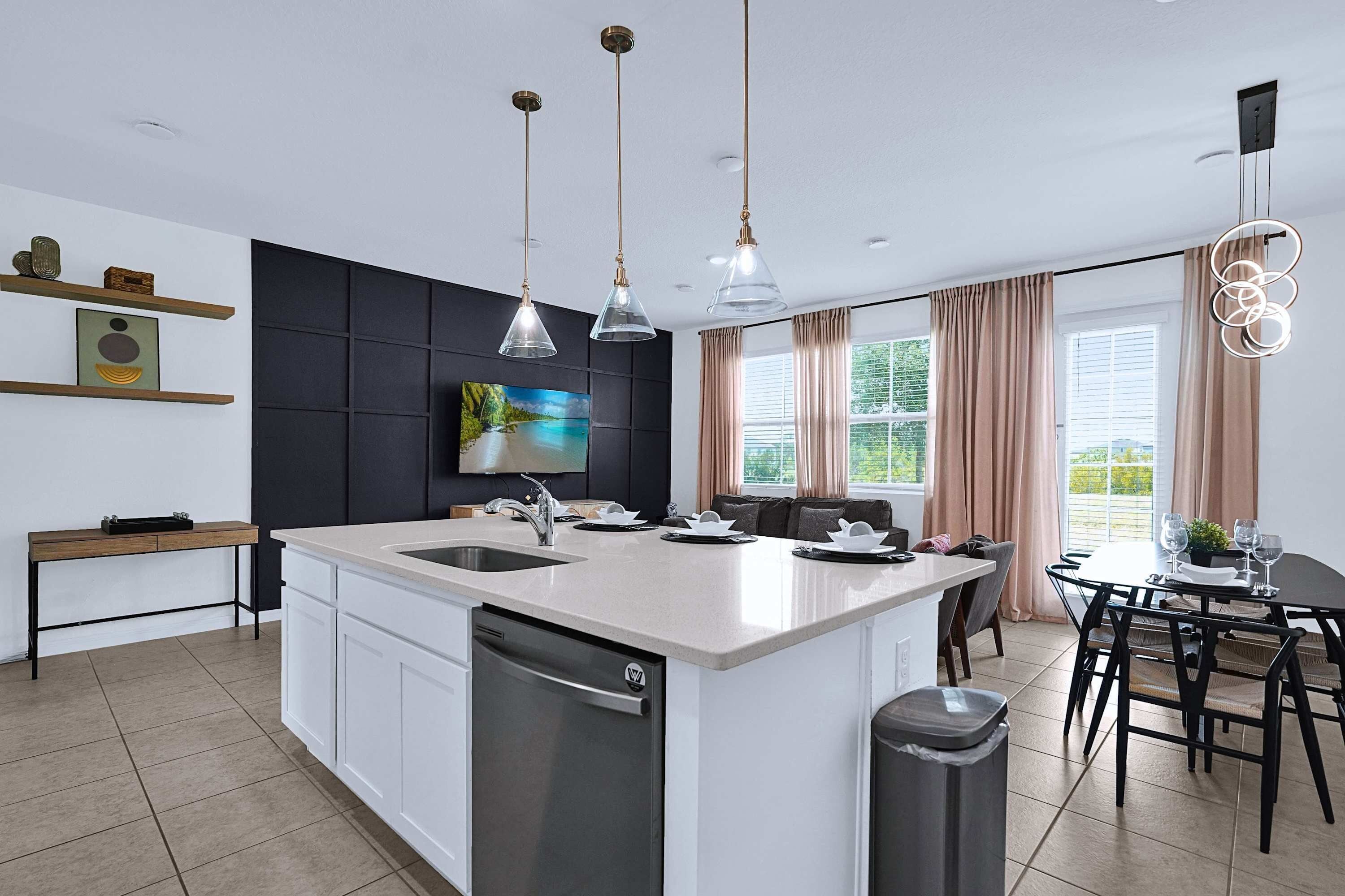 A modern kitchen with a central island, pendant lights, a dishwasher, and a dining area with a table and chairs.